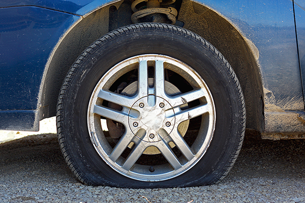 close up of a flat tire of a rusty old blue car centered on gravel road
