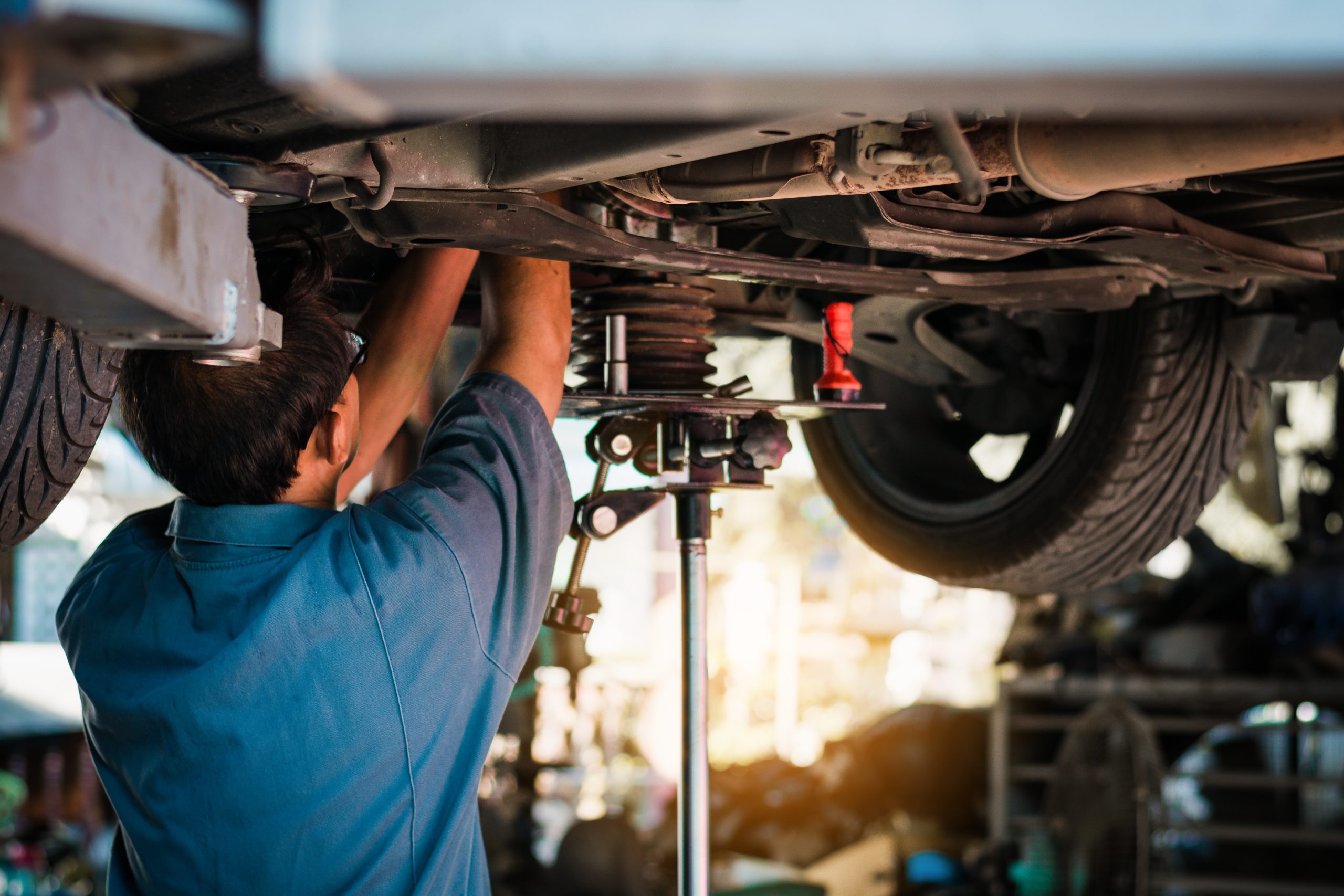 Mechanic working on a car's suspension system under the car.