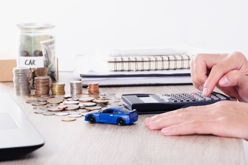 Hand using calculator, jar of change, loose money, and a notebook